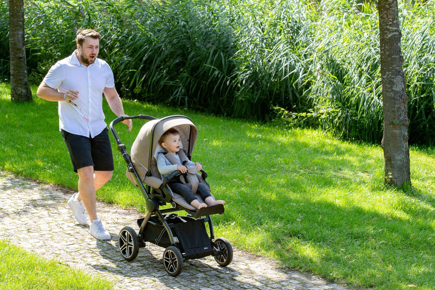 Vater mit Kind im Kinderwagen im Grünen