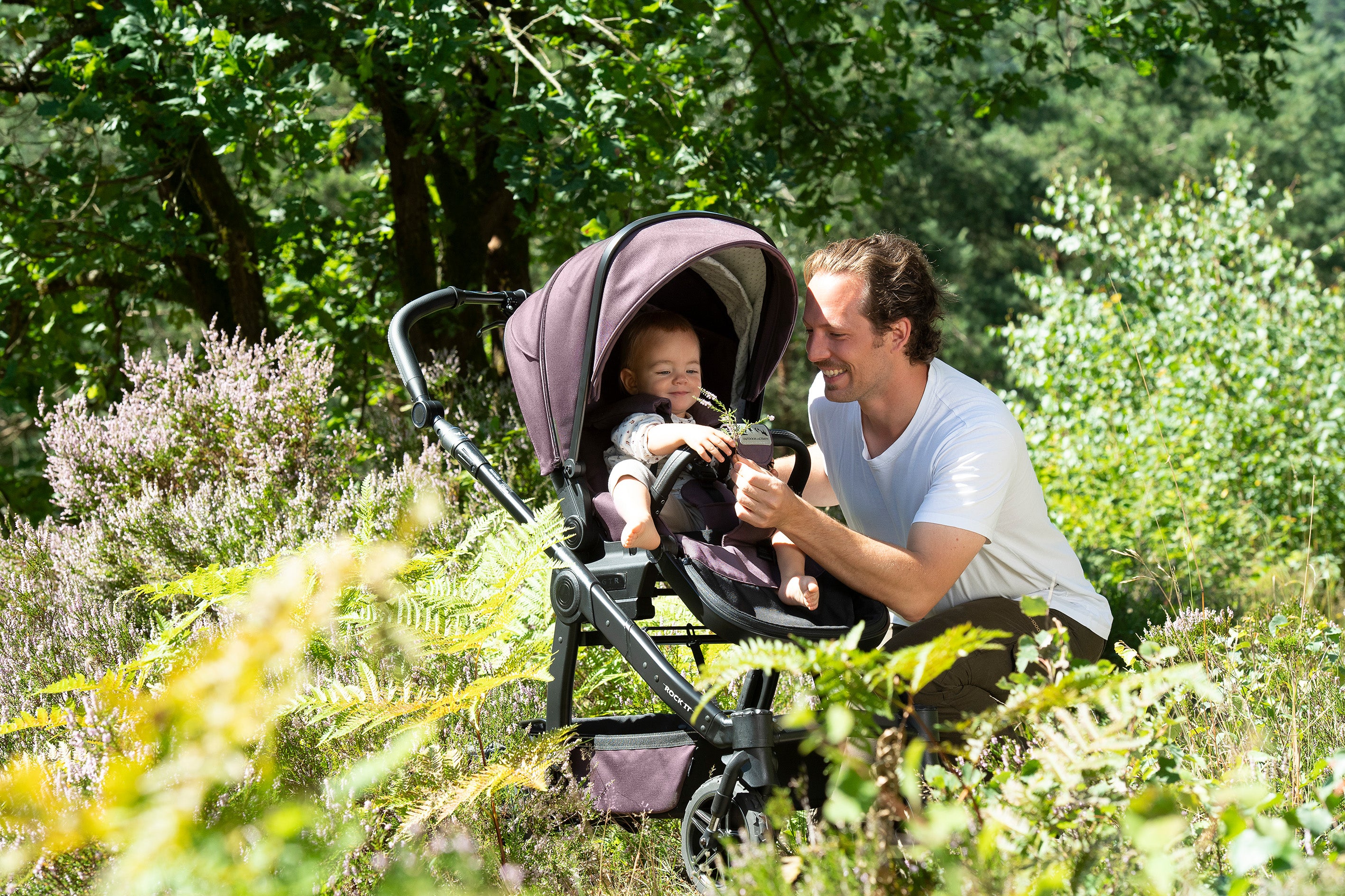 Vater mit Kind im Kinderwagen im Grünen