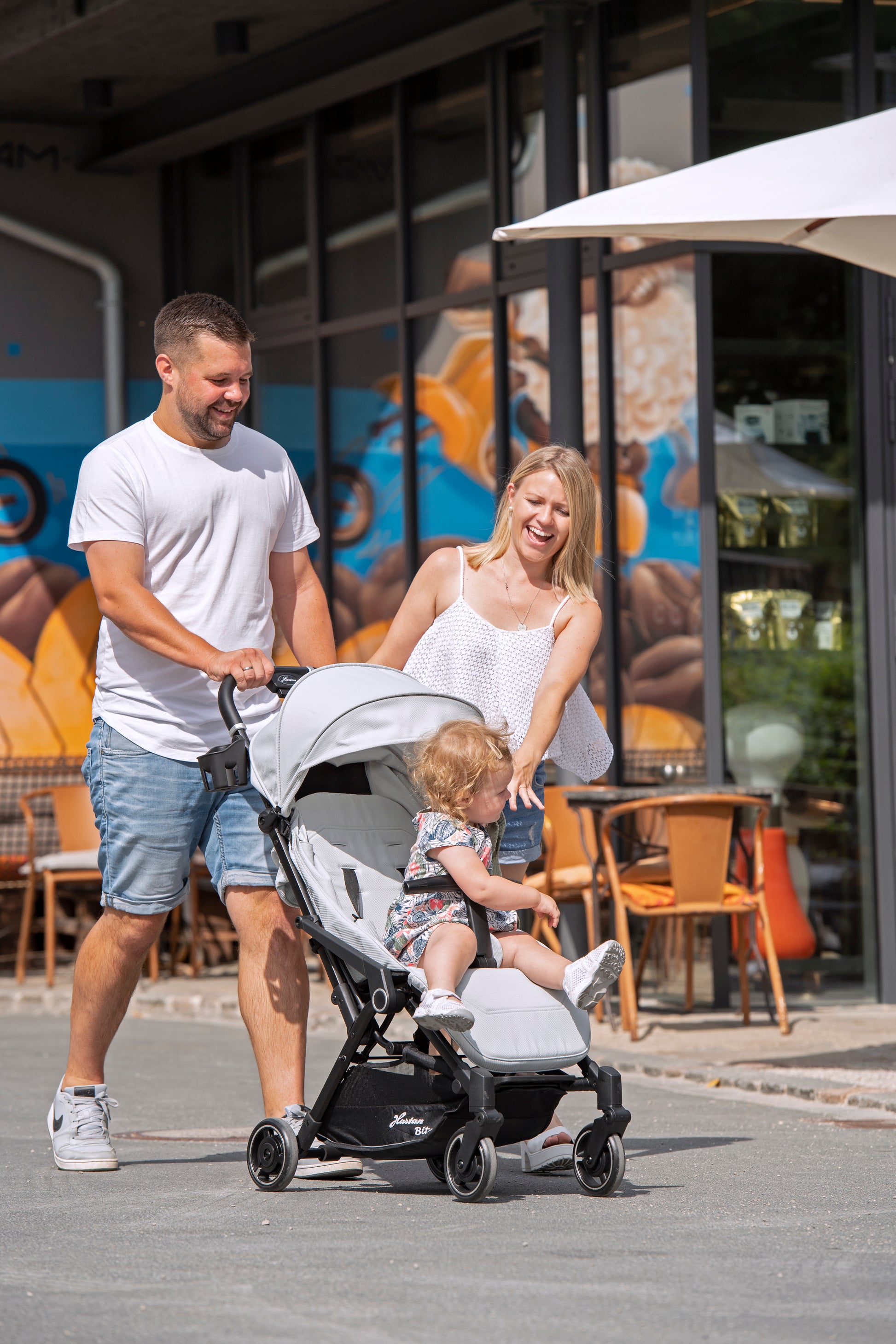 Eltern mit Kind im Buggy gehen an einem Café vorbei